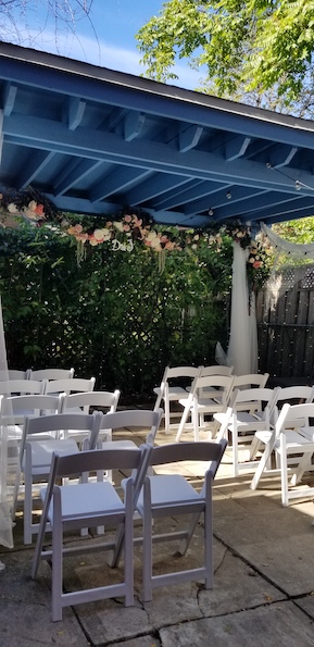 white resin chairs with padded seats set up in 5 rows of 4 with 2 chairs on either side of the aisle underneath structure