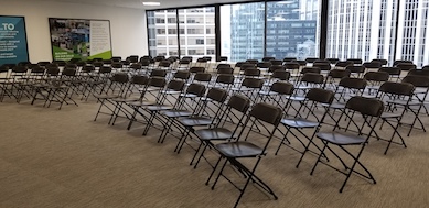 Black Plastic with metal folding chairs set up in rows in downtown venue with full glass windows in the background showing view of downtown 