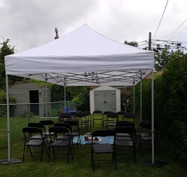 10 foot by 20 foot tent with about 20 black metal with vinyl padded chairs under it and floor covering set up for ceremony in backyard