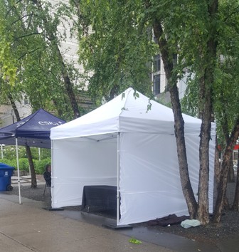white pop up tent with 3 walls and table with black tablecloth set up under it in Yorkville next to tree and other third party tent 