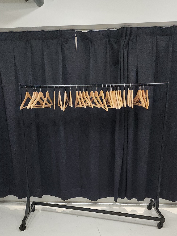 black metal rolling z style rack with wooden hangers on concrete with black drape in background